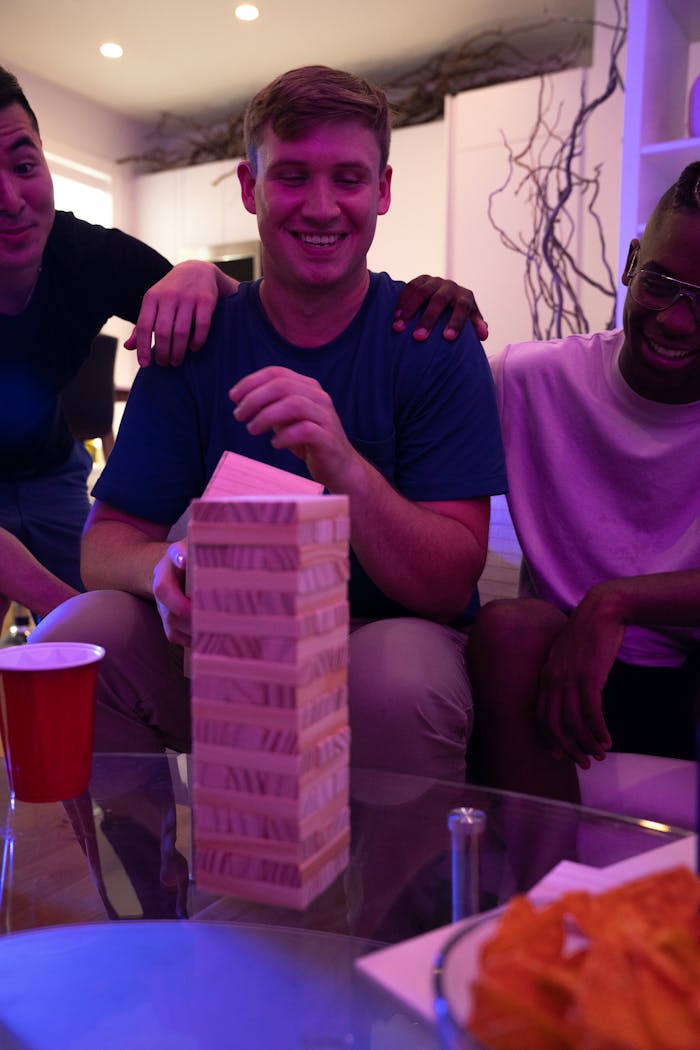 Three friends enjoying a fun game of Jenga indoors with snacks and drinks.
